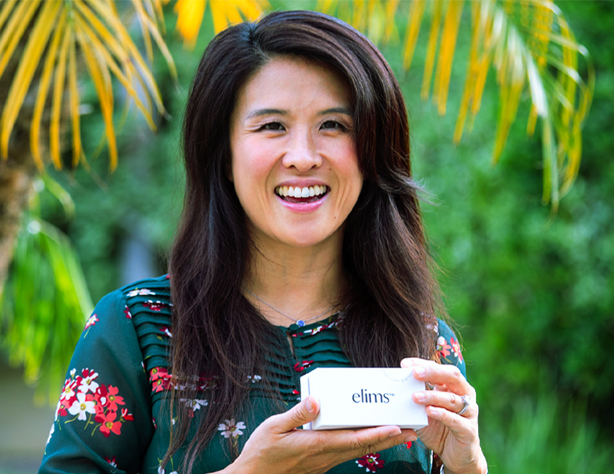 A woman in a floral shirt holds a box with "ELIMS" written on it.
