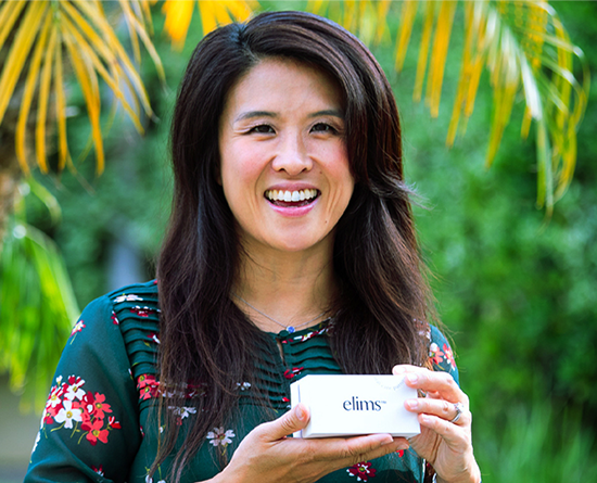 A woman in a floral shirt holds a box with "ELIMS" written on it.