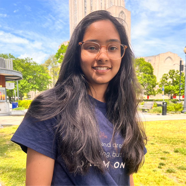 A young woman in an indigo shirt stands on a grassy plaza.