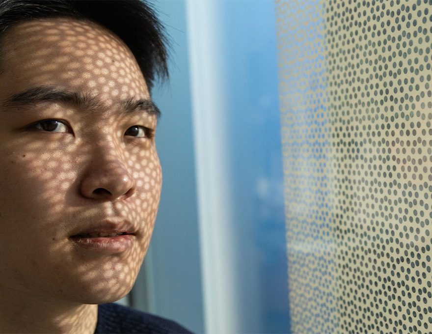 A man stands near a window. Over the window is a filter with several holes punched into it. 